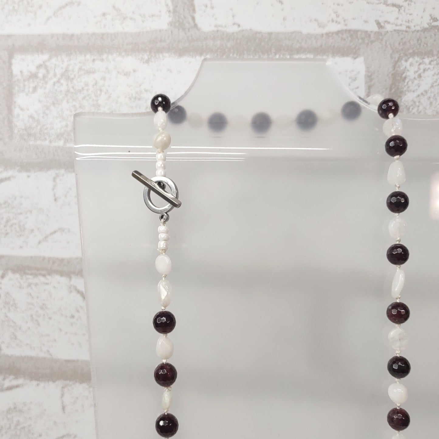 Large Faceted Garnet Beads and Moonstone nugget beads strung on 100% silk cord hand-knotted to separate each bead and finished with a stainless steel toggle. close up of toggle clasp